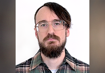 Headshot of a man with a mustache and beard wearing glasses