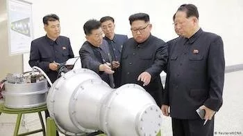 North Korean leader and officials standing around a bomb talking and pointing.