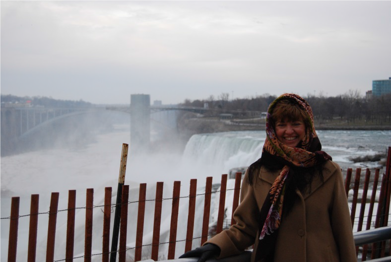 Woman in winter attire standing for the camera in front of a large waterfall.