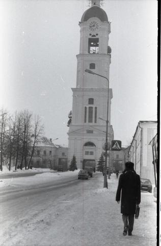 Snowy day with a street leading to a tower and people walking.