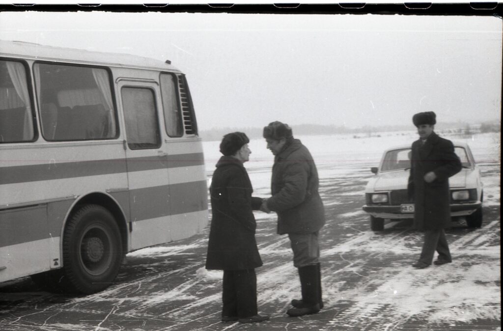 Two men shaking hands outside in front of a bus with snow in the background