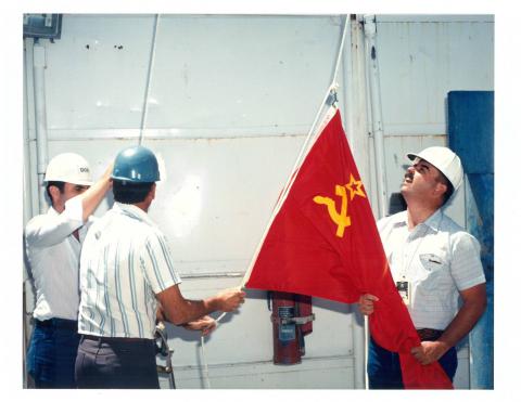 Men with hard hats raising a flag.