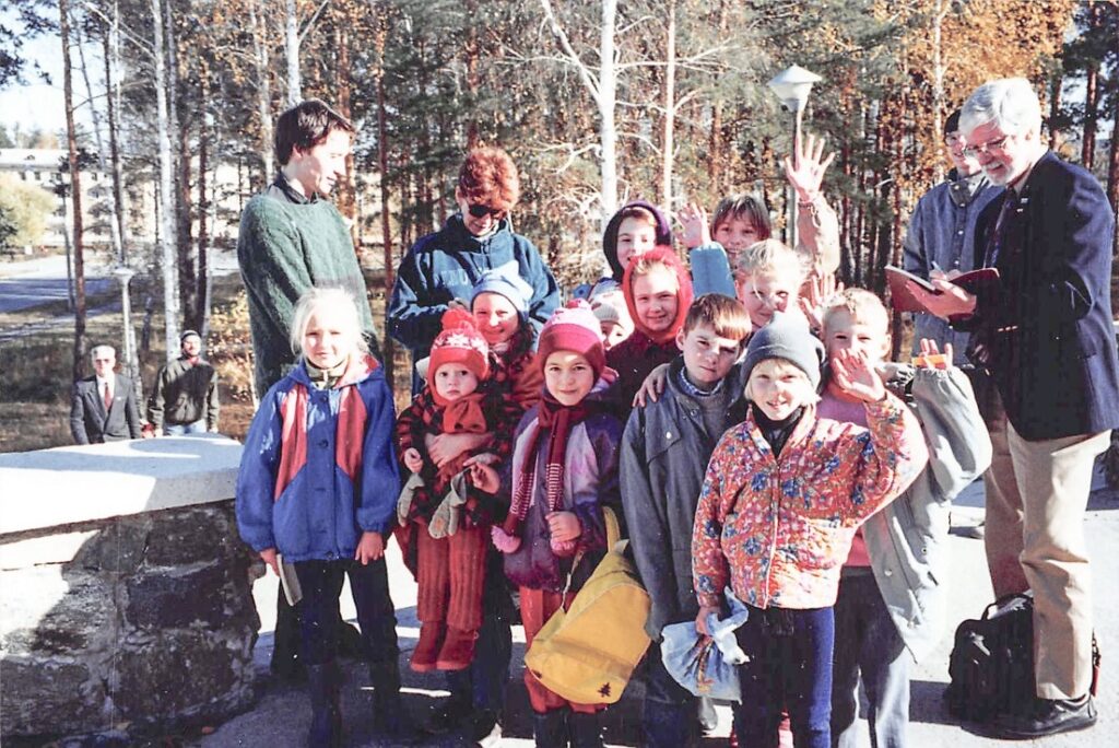 A bundled up group of children with two adults smiling and waiving at the camera on a cold day