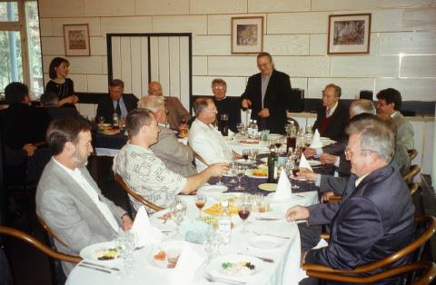 People seated around a table with a man standing giving a toast 