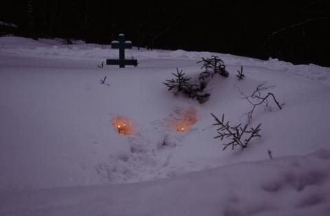 Twilight with a cross and lit candles mostly buried in snow.