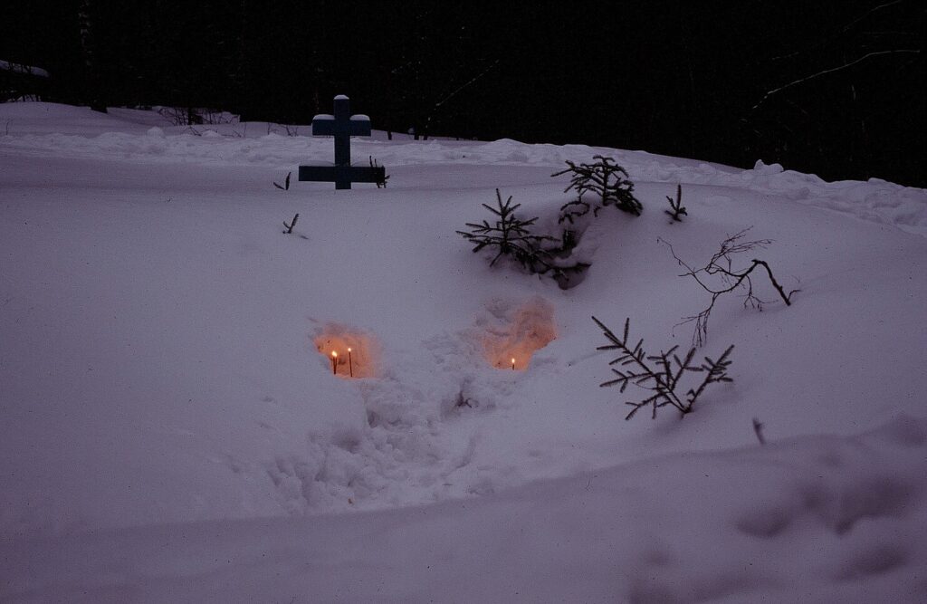 Candles embedded in the snow with a cross above them and branches poking out of the snow