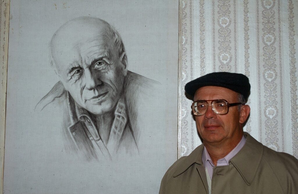 Man stands in front of a sketched portrait of another man