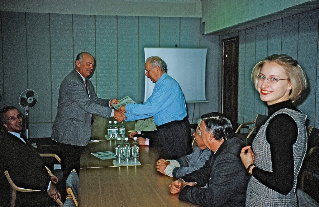 Group around a table with two people at the head, one giving the other the certificate
