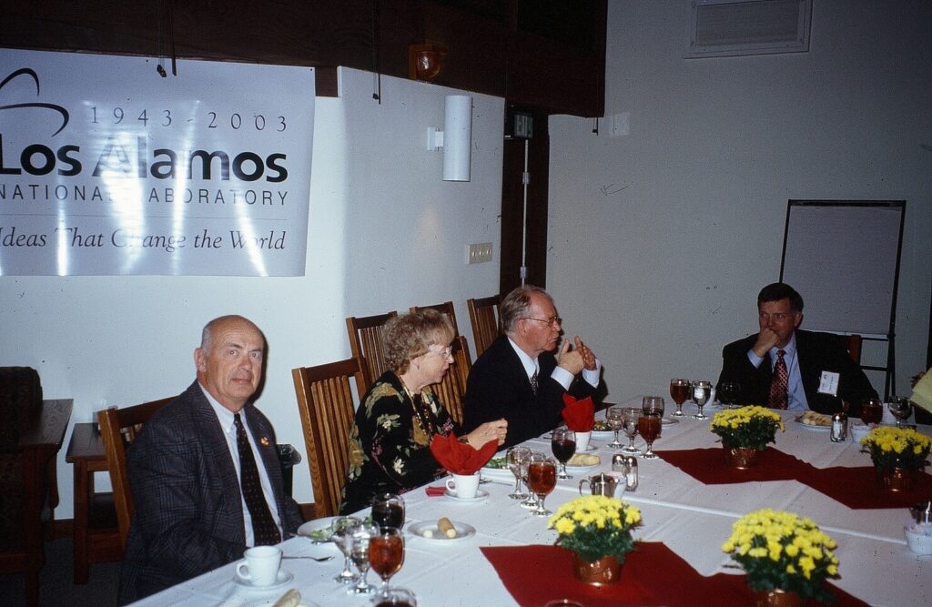 People sitting at a table in suits with yellow flowers.