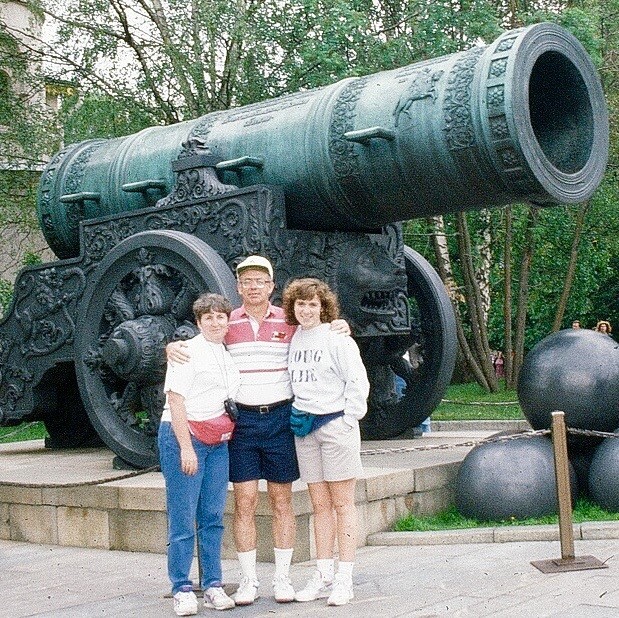Family of three in front of a cannon in a park like setting.